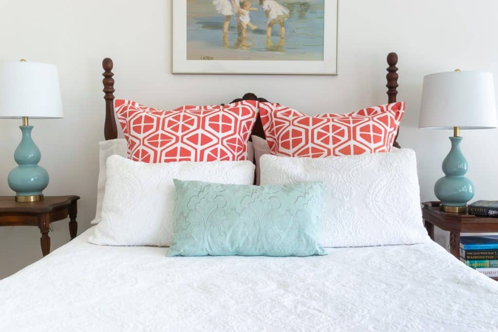 Bed with orange and white pillow shams, white pillows and pale blue pillow..