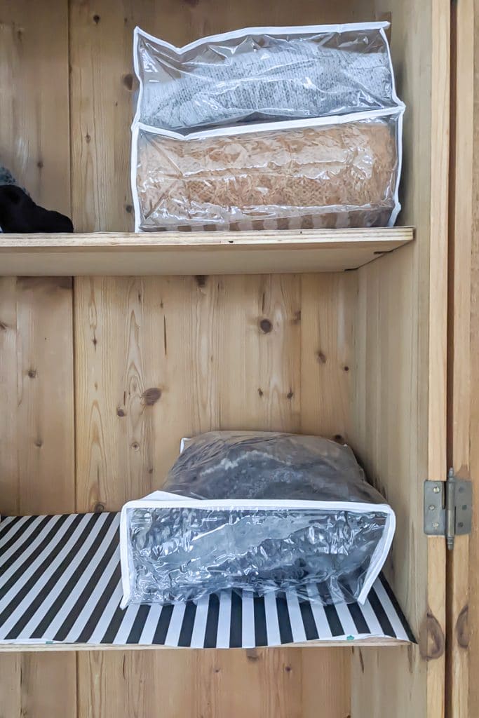 Sweaters in plastic bags in a wooden cupboard.