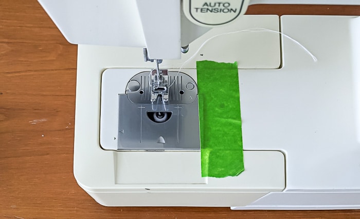 placing a piece of tape on sewing machine to edge flange.