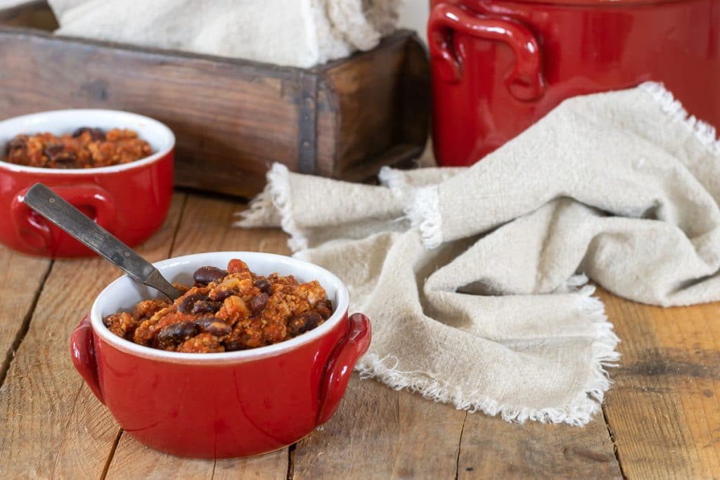 Hearty Crockpot Turkey Chili in a red bowl in front of a large red pot of chili.
