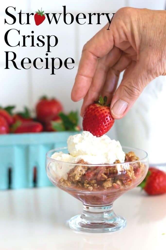 Putting a strawberry on top of a bowl of strawberry crisp and whipped cream.