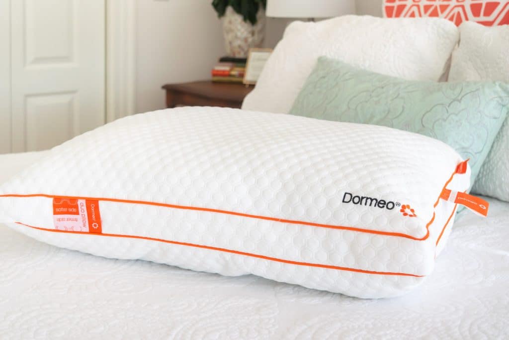 A white pillow with orange piping on a bed.