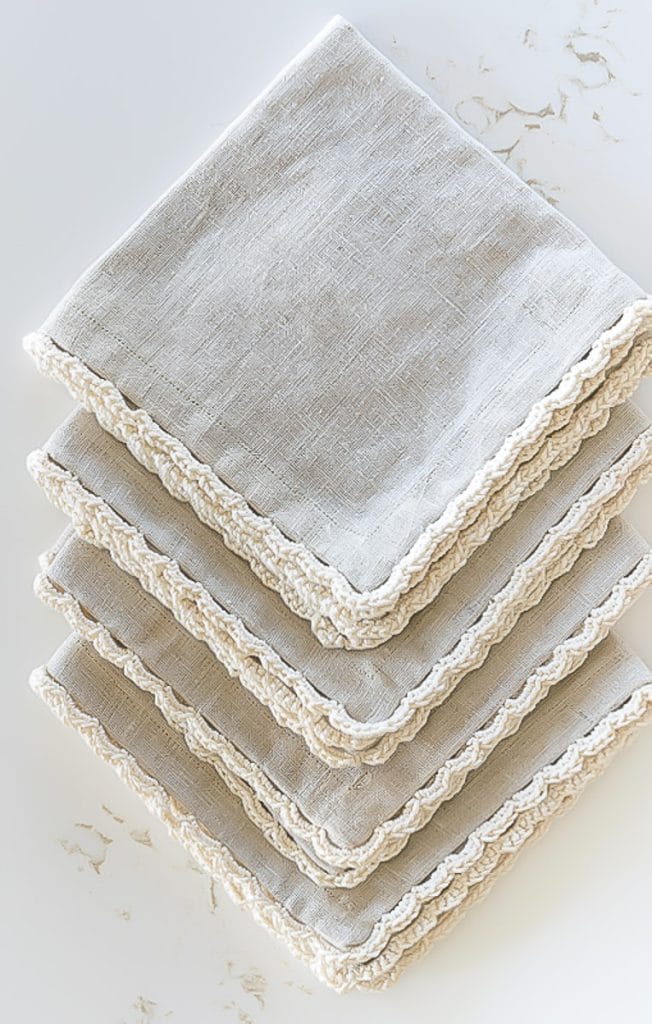 Four beige linen napkins with off-white crochet edging.