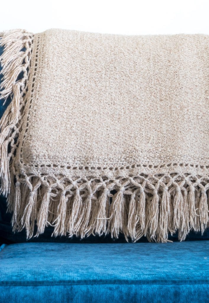 A beige knit throw with fringe.