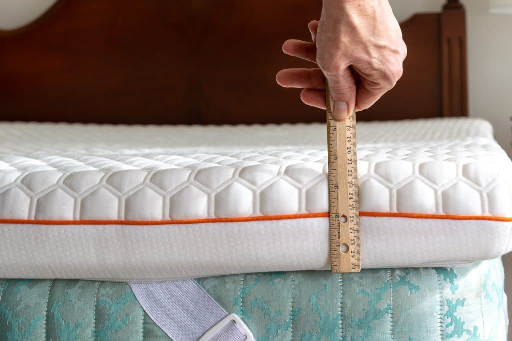 A hand measuring the thickness of a foam mattress pad.