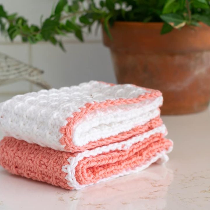 White and peach knit washcloths with a potted plant in the background.