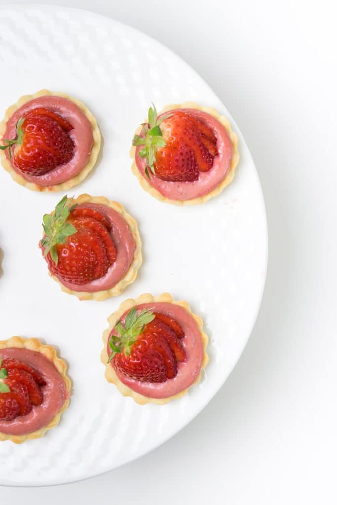 Strawberry curd tarts with fresh strawberries on a white cake plate.