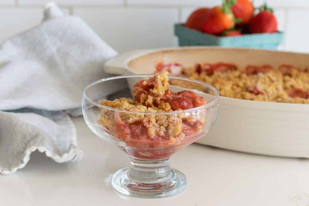 A baking dish of strawberry crumble recipe with a small bowl of strawberry crumble.