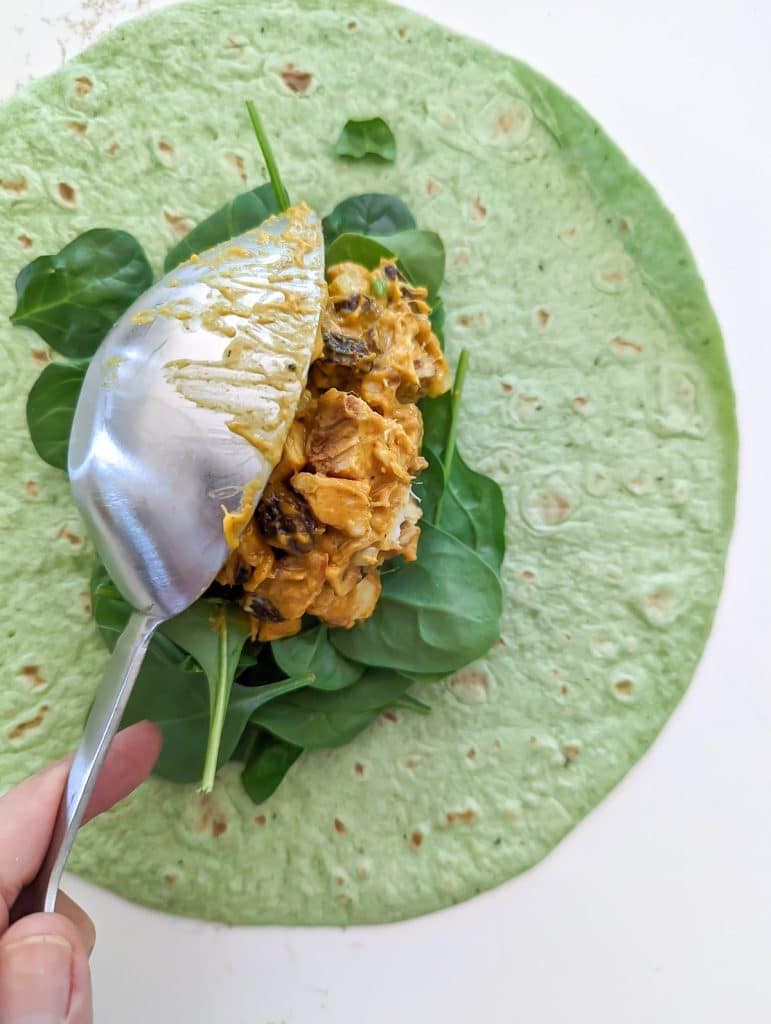 A sccop of curried chicken salad on a bed of spinach and a spinach wrap.