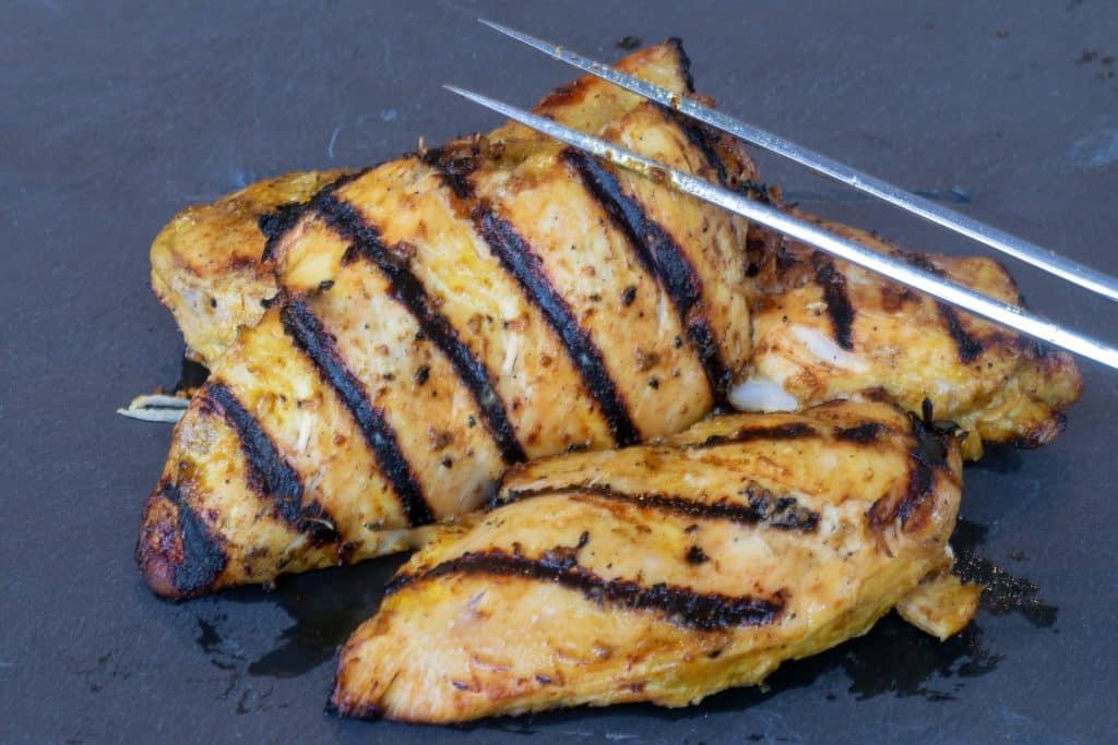 Two pieces of grilled chicken on a piece of slate