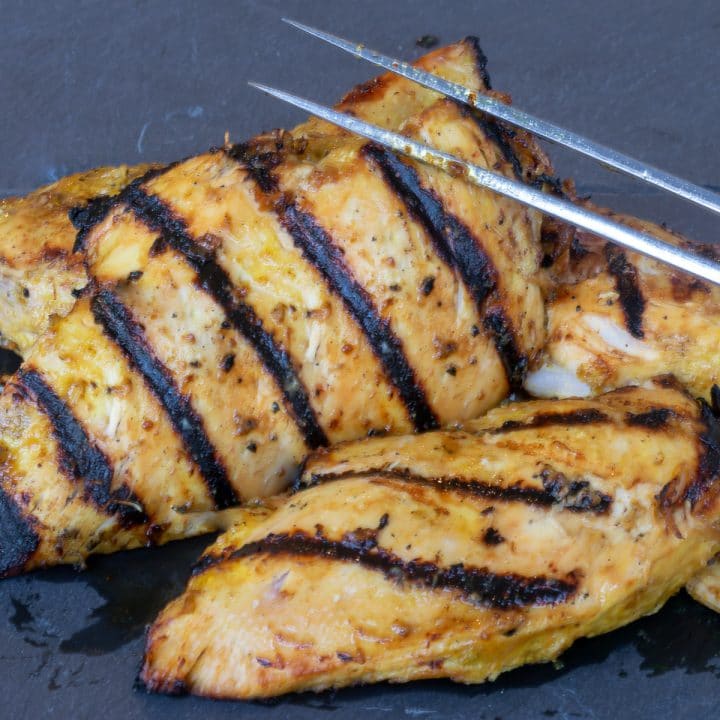 Two pieces of grilled chicken on a piece of slate