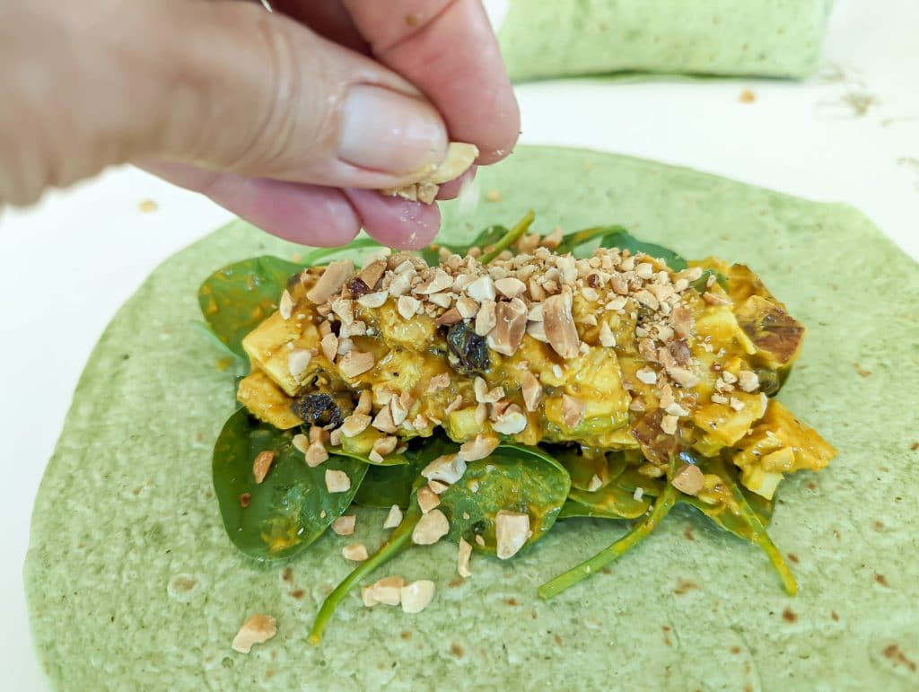 Sprinkling peanuts on a Curried chicken salad wrap