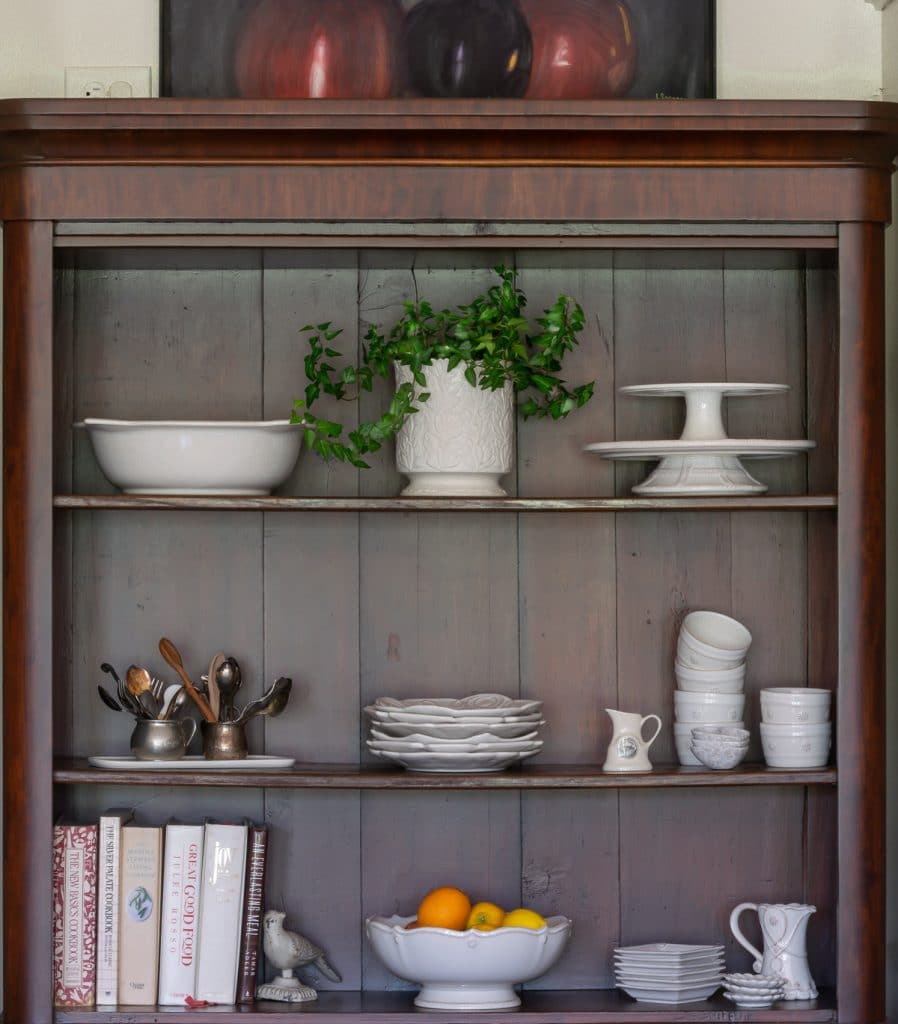 Wooden hutch with white pieces and a plant on the top shelf
