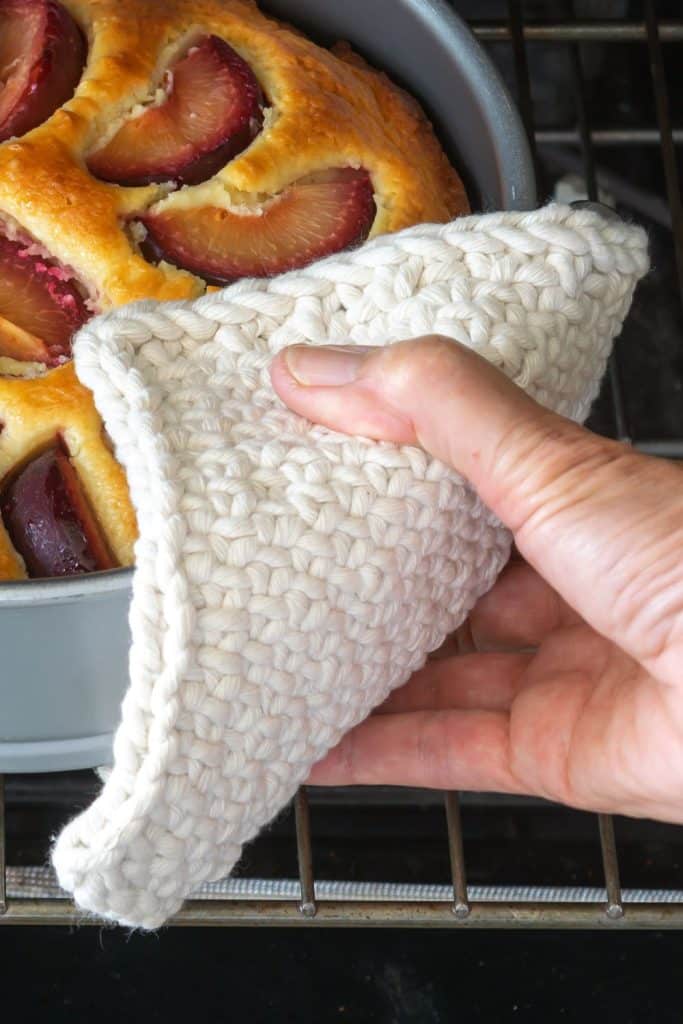 Hand using knit potholder to pull cake from the oven.