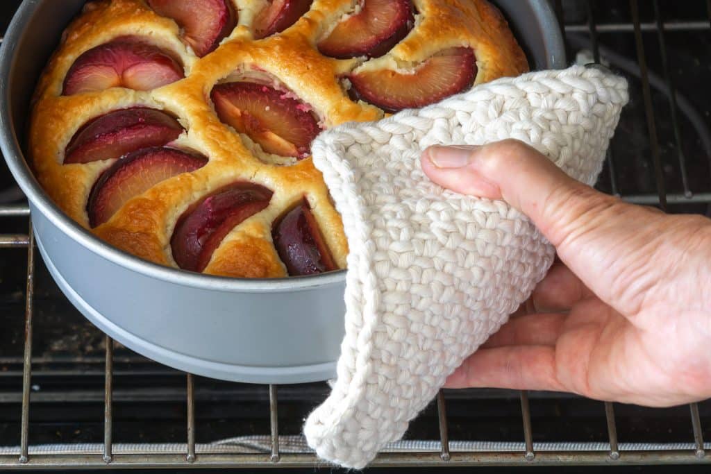 Knit potholder pulling hot cake from oven.