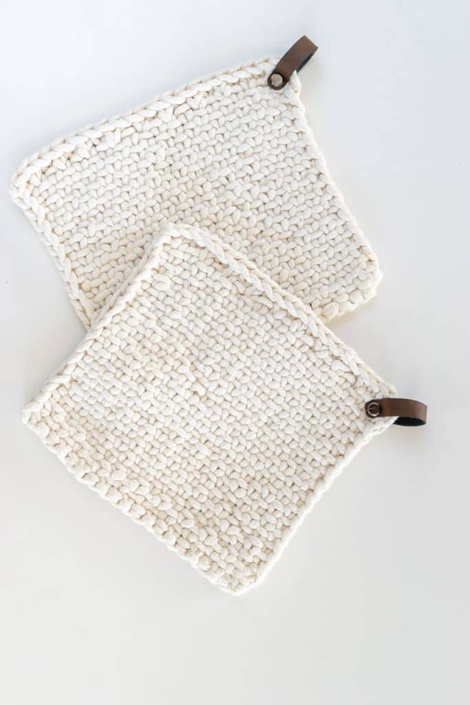 Two white knit potholders on a white counter.
