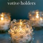 Three beaded wire macramé votive holders with lit candles inside.