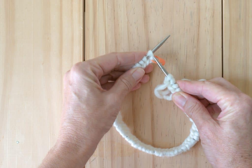 Begin knitting in the round by holding the needle with the tail of the working yarn in your right hand.
