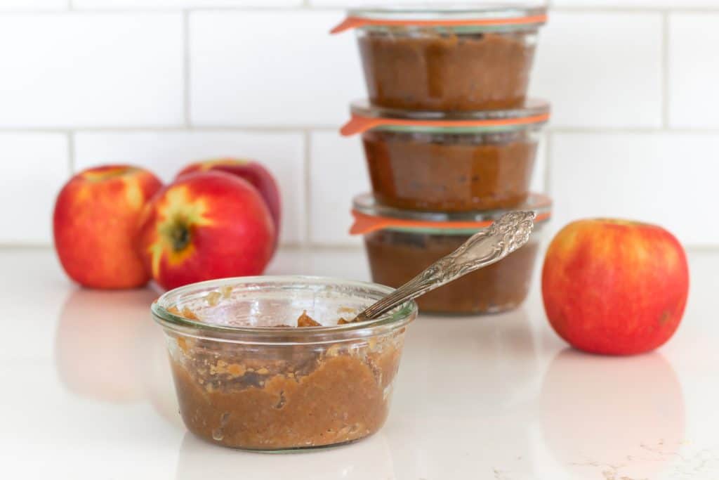 A stack of jars filled with sugar-free apple butter, with a few fresh apples.