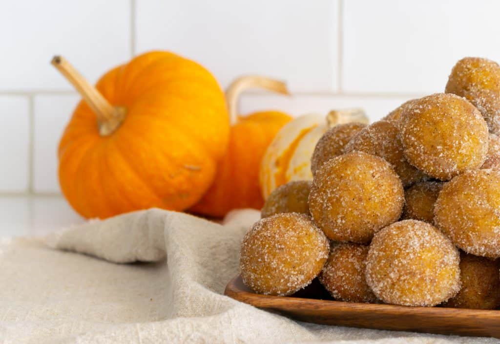 Stack of Baked Pumpkin Donut Holes on a wooden tray.