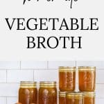 Jars pf homemade vegetable stock with fresh vegetables scattered around.