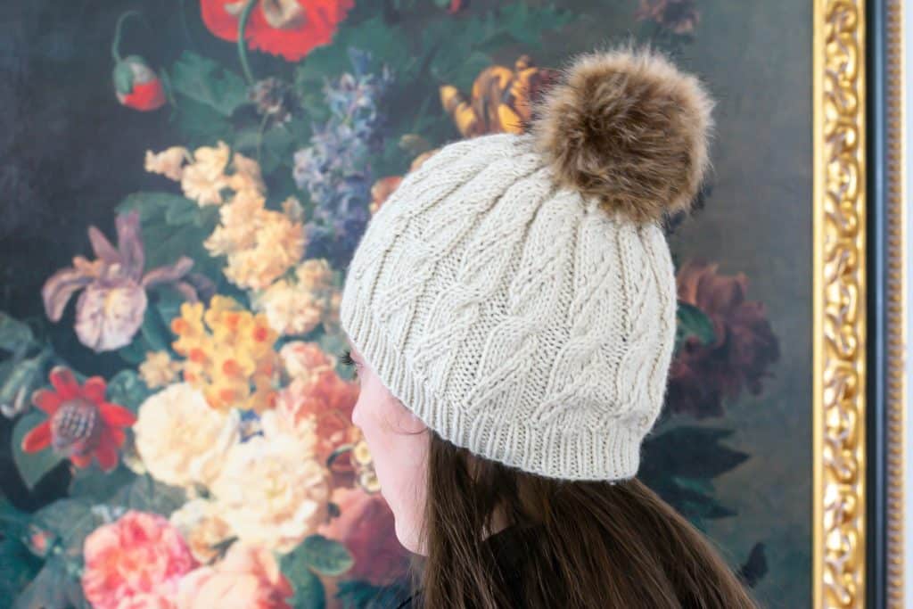 Girl wearing cable knit hat in front of painting.