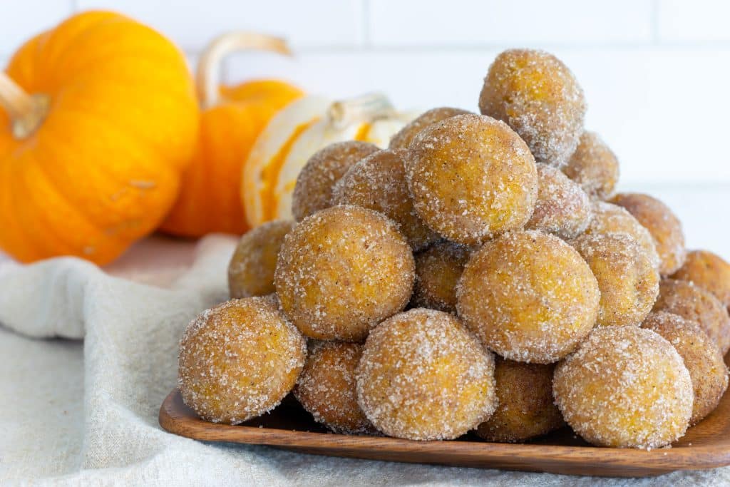 Stack of pumpkin spice donut holes on a wooden platter.
