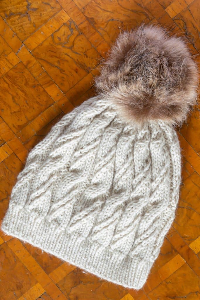 A knit hat with a fur pom pom on a table.