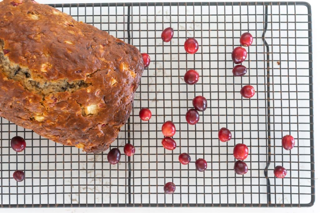 Apple, Cranberry and Banana bread on a rack with scattered cranberries.