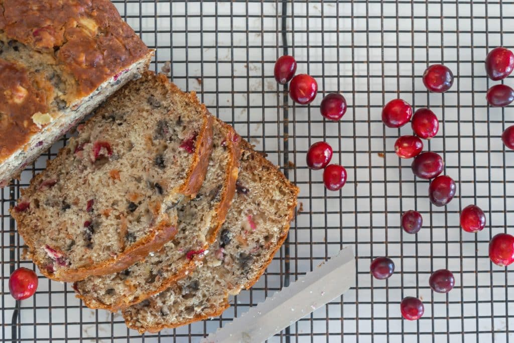Sliced Cranberry Apple Banana bread on a cooling rack, with fresh cranberries sprinkled around.