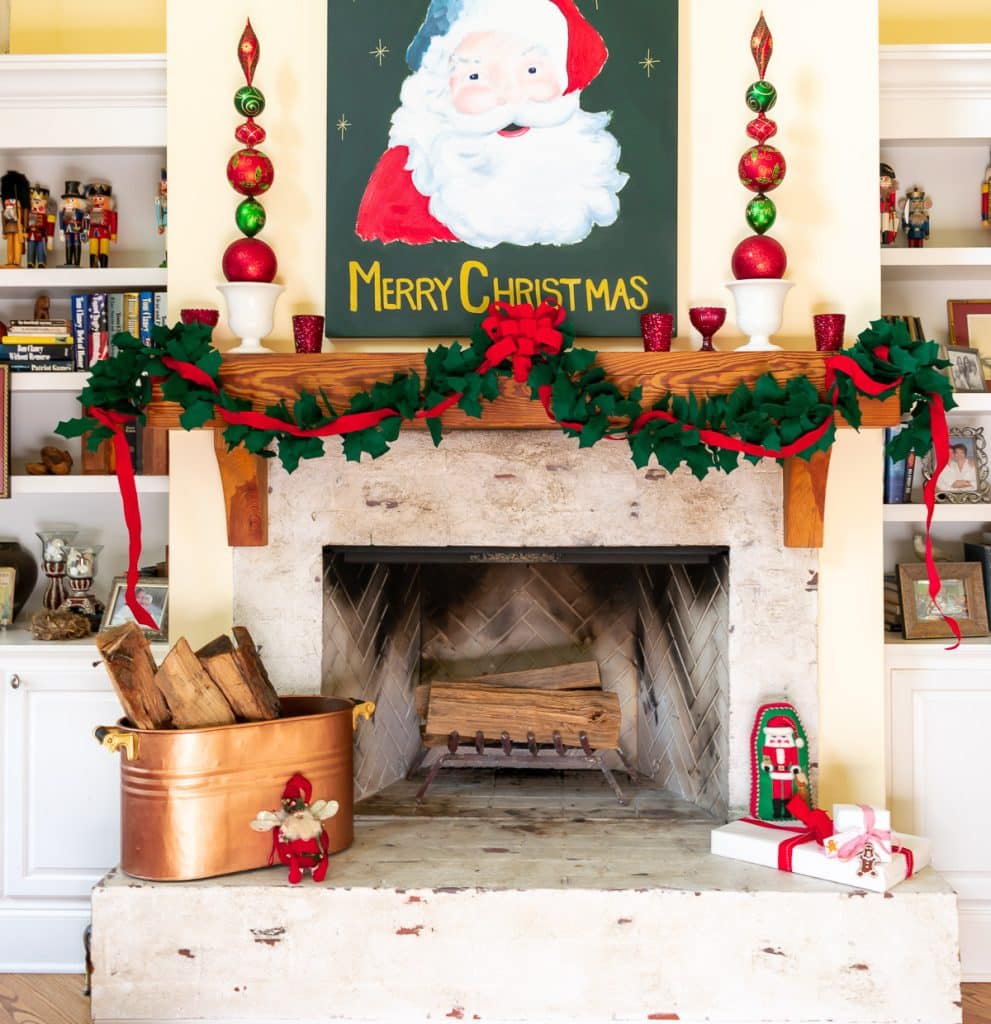 A Christmas fireplace with a santa painting, garland on the mantel and tall ornament topiaries.