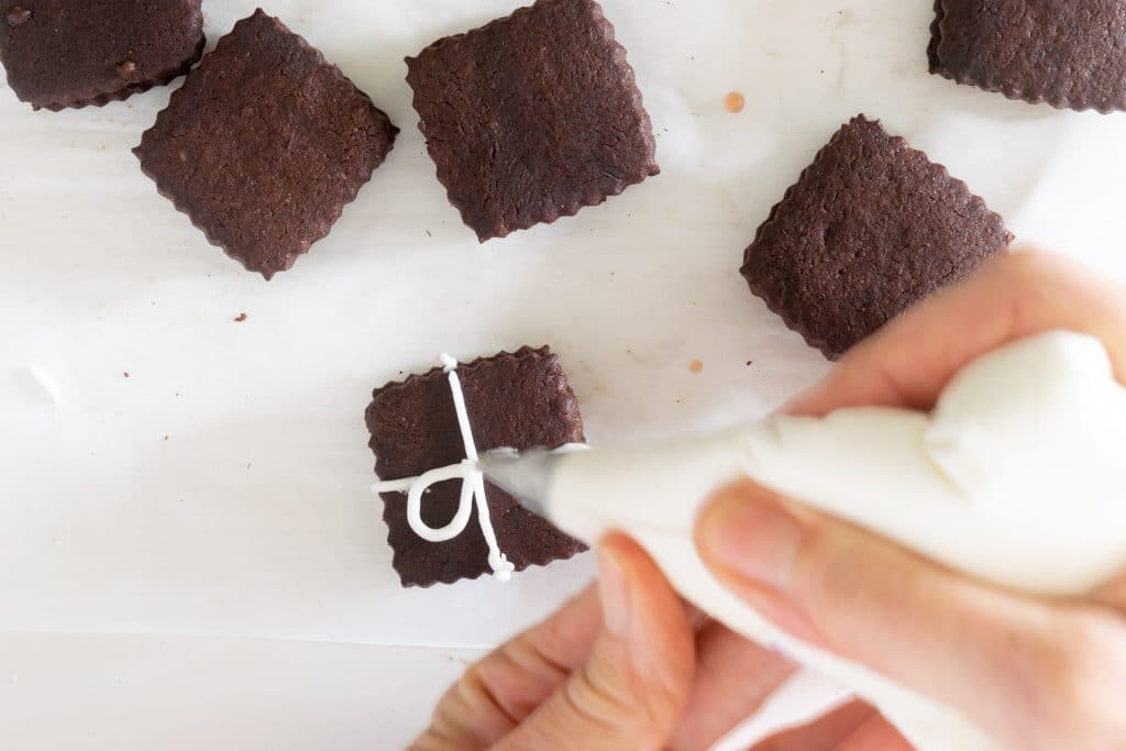 Piping ribbon on chocolate sugar cookies.