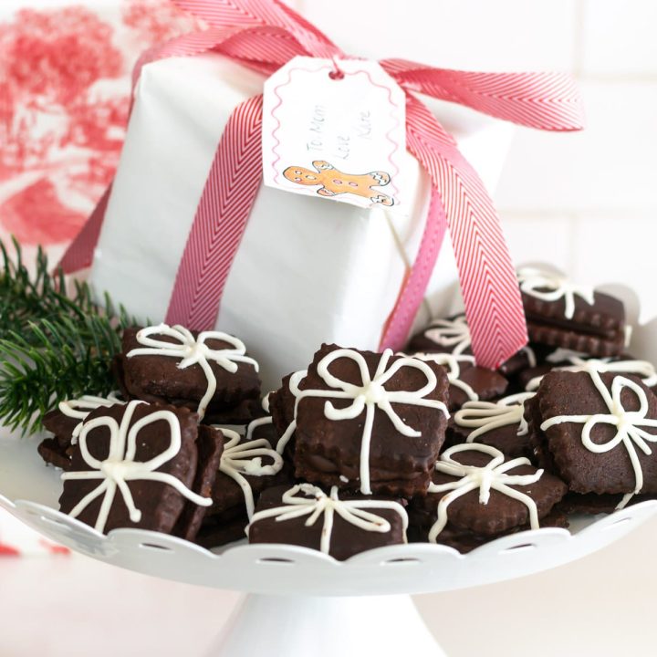 Chocolate Sugar Cookies that look like presents on a tray with a white box wrapped in a pink/red ribbon.