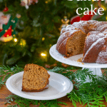 Gingerbread bundt cake on a pedestal in front of a tree with a slice of cake on a plate.