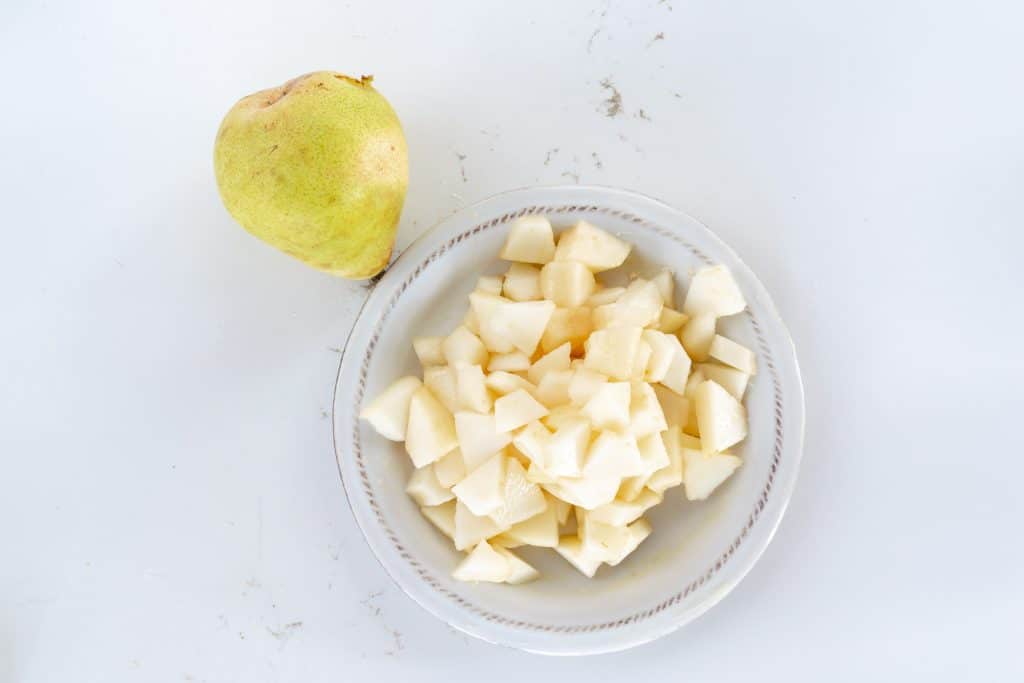 A bowl of diced pear and whole pear.
