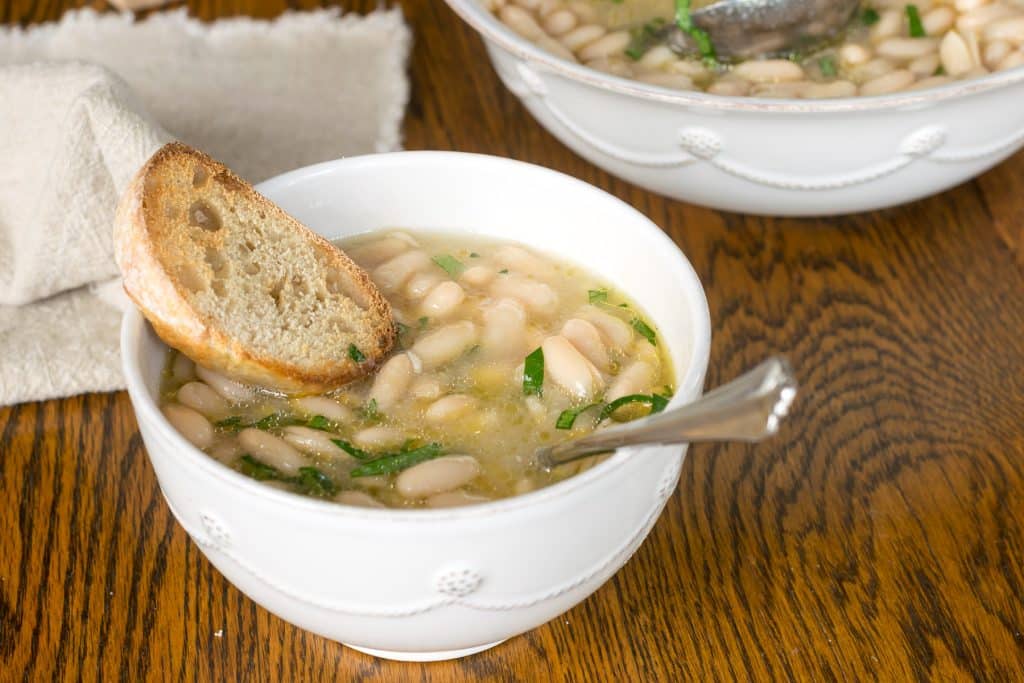 Bowl of brothy beans with a piece of bread and a spoon.