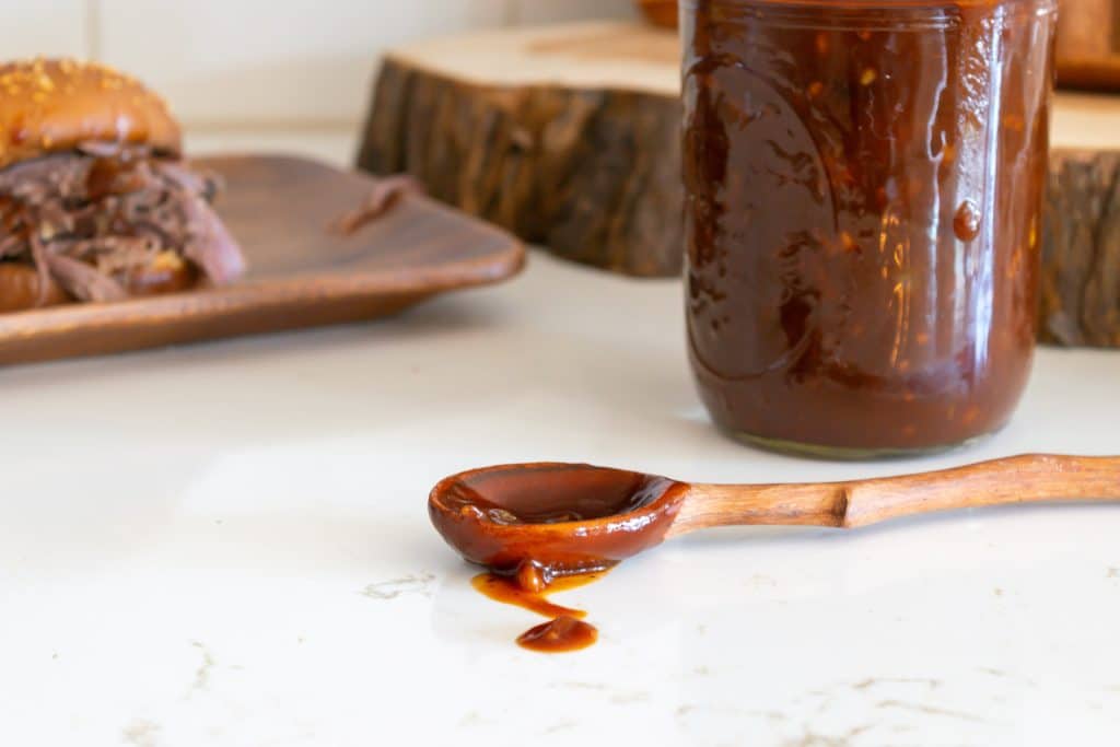 BBq sauce in a jar with a wooden spoon.