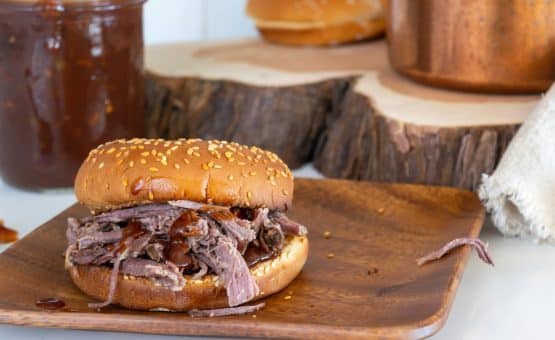 A bbq sandwich sitting on top of a wooden plate.
