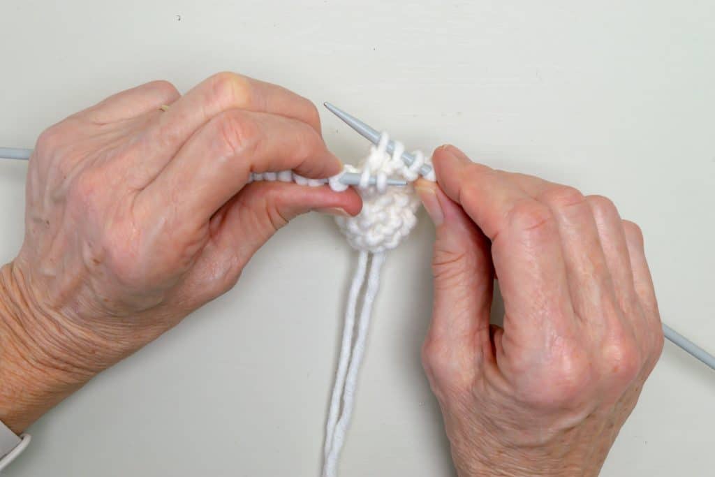 Hands holding knitting needles and knit fabric.
