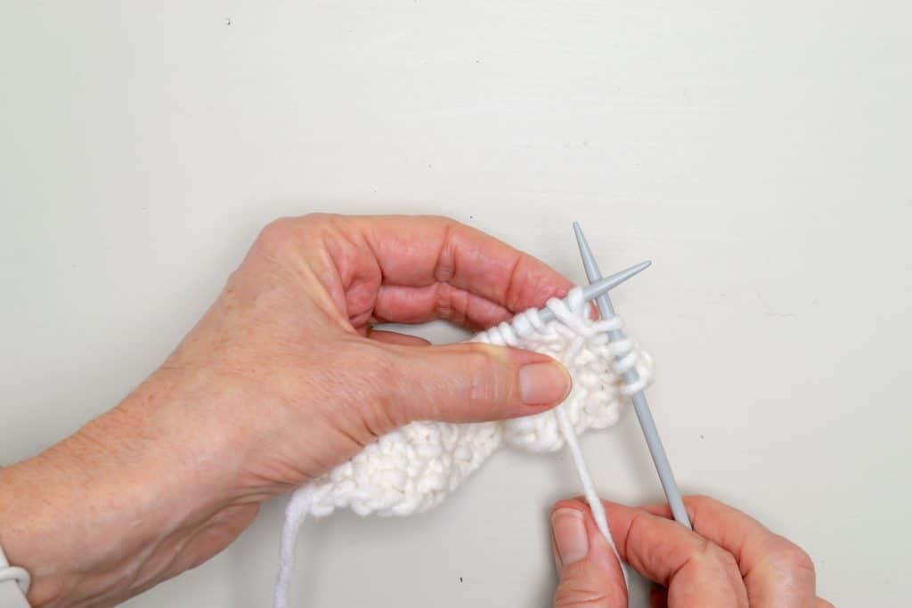 Hands holding knitting needles and knit fabric.