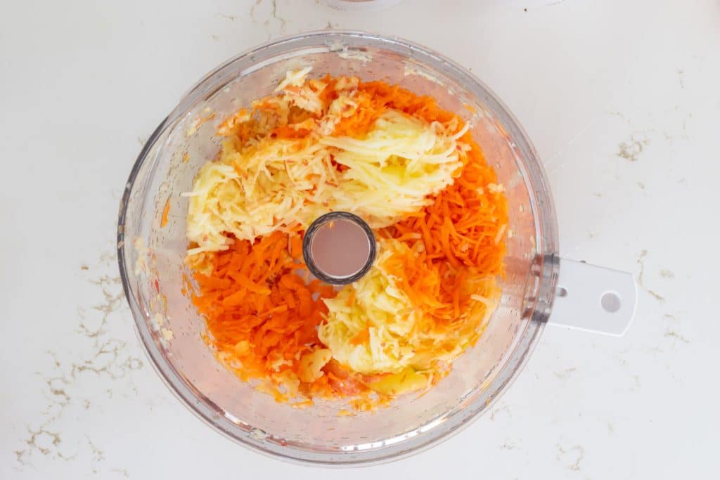 Grated carrot and grated apple in the bowl of a food processor.