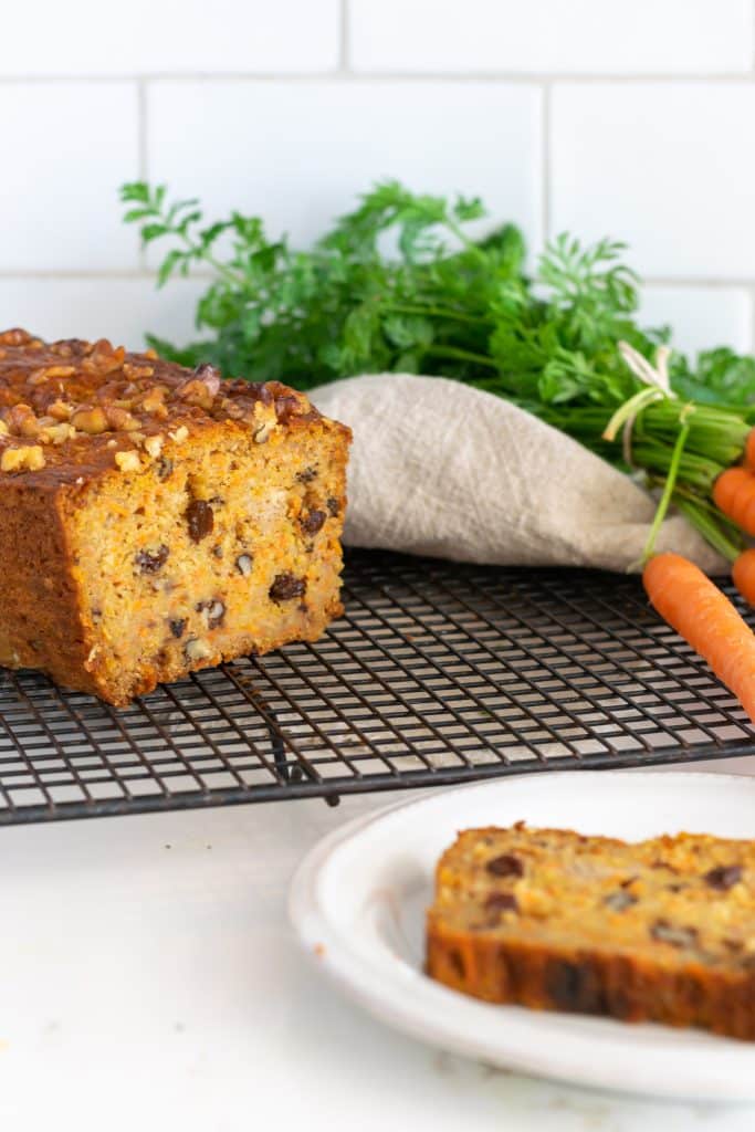 Carrot bread loaf  on a cooling rack with fresh carrot in the background.