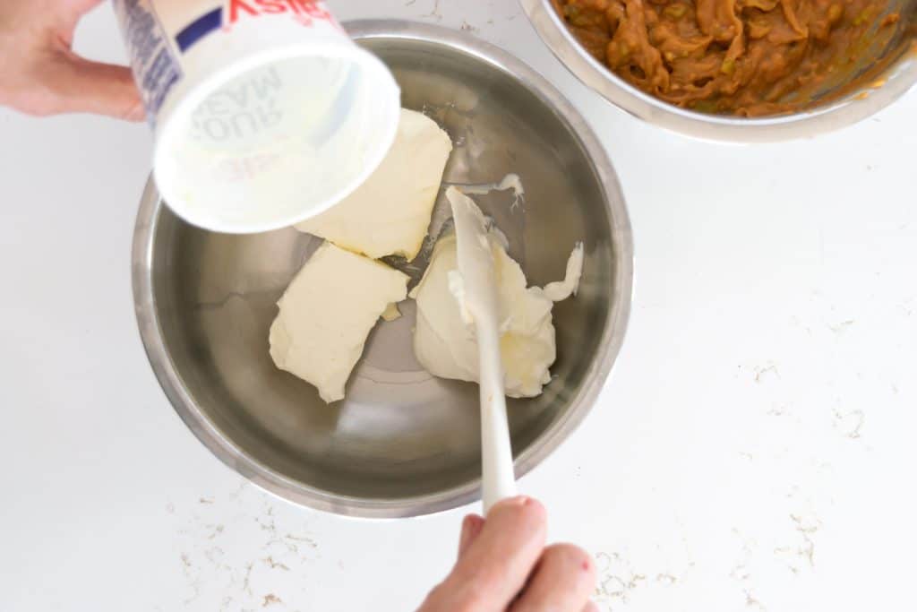 Adding sour cream to cream cheese in a bowl.