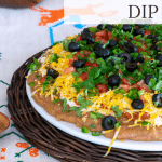 Layered Taco Dip on rattan platter on tablecloth.