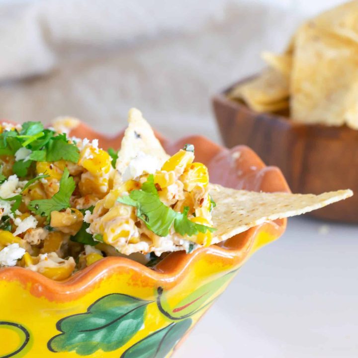 Elote dip in a yellow Mexican bowl with a chip for dipping.
