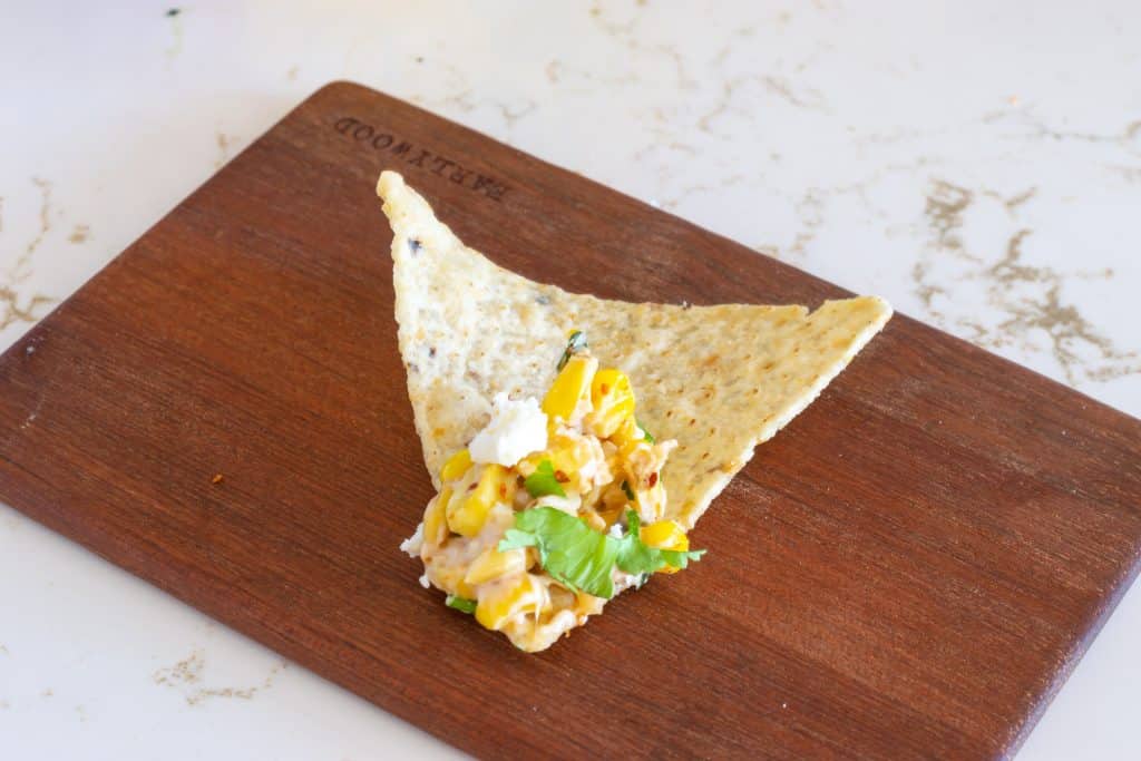Elote dip on tortilla chip on a wooden plate.