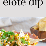 A bowl of elote dip with a tortilla chip that has elote dip on it.