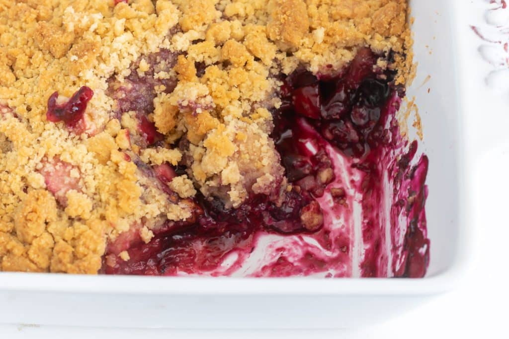 White baking dish with apple and blueberry crumble, with a scoop of dessert removed.