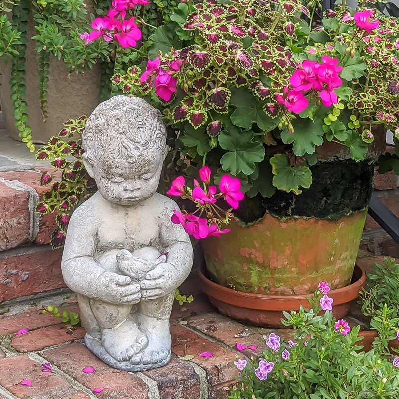 Statue of a little boy on brick steps with a container pot in the background.