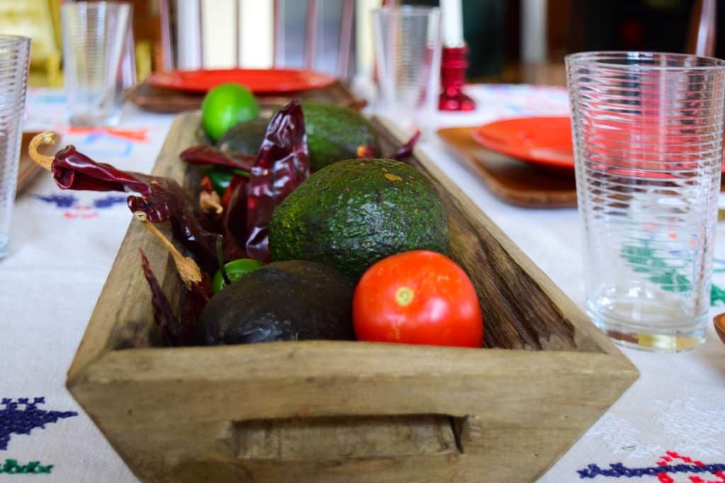 A long wooden rectangular box with avocados, tomatoes and dried chiles.